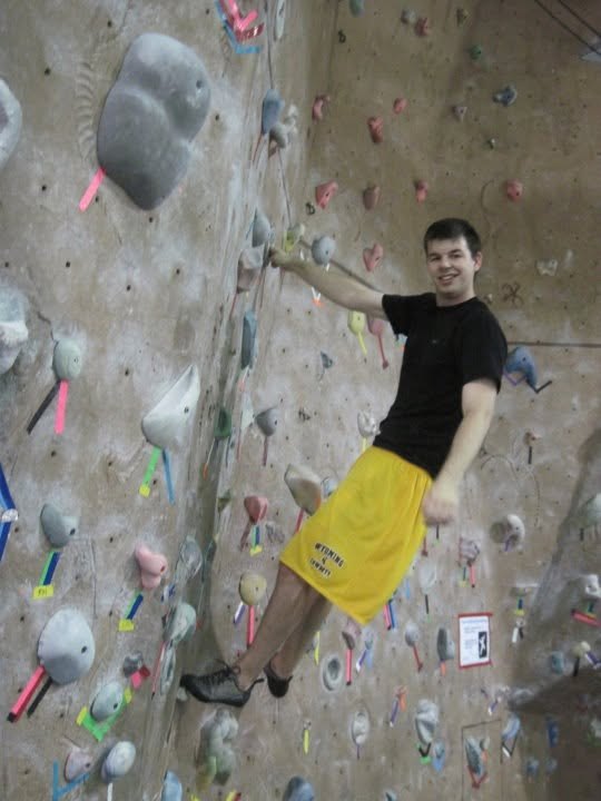 Casey on an indoor climbing wall, wearing University of Wyoming shorts
