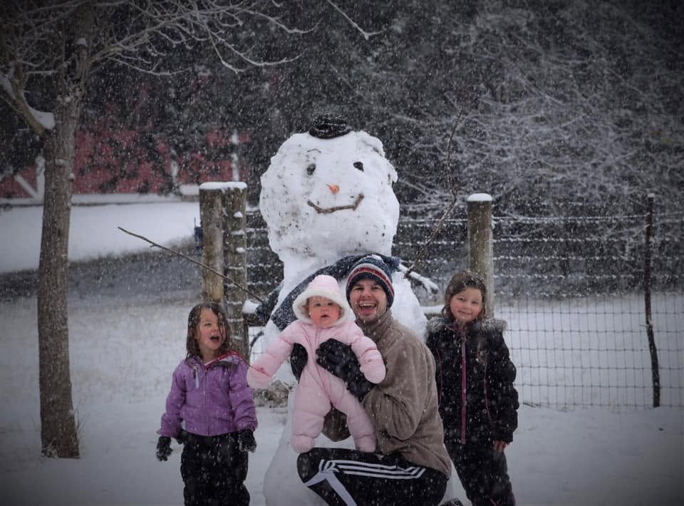 Casey and his three daughters in front of a big snowman on a snowy day