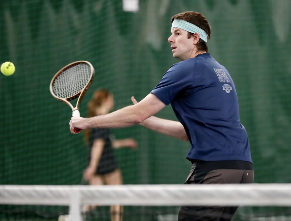 Casey hitting a backhand volley on an indoor tennis court